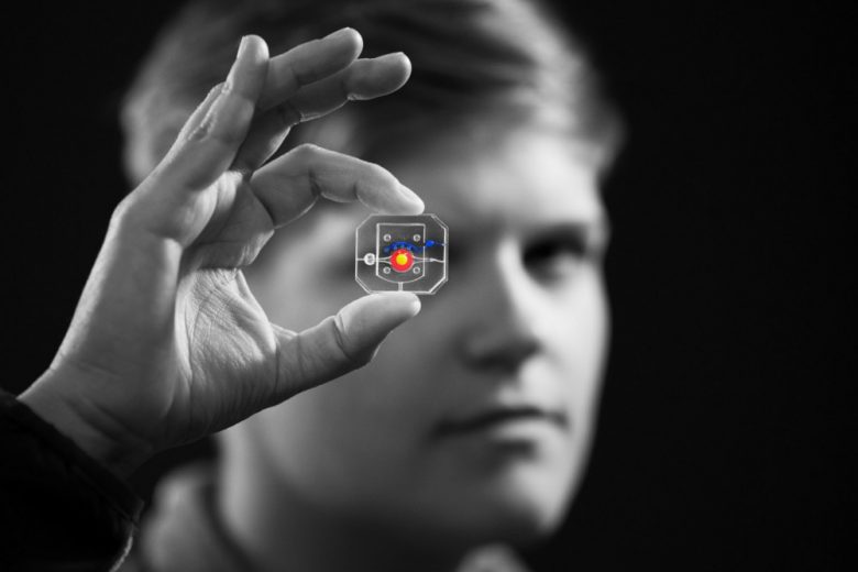 Man holds up eye-on-a-chip between thumb and forefinger