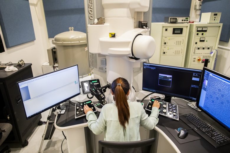 Researcher sits at dual monitor desk in nanomaterial research lab