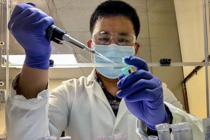 Research assistant Jinzhao Song works in lab, wearing face mask and gloves