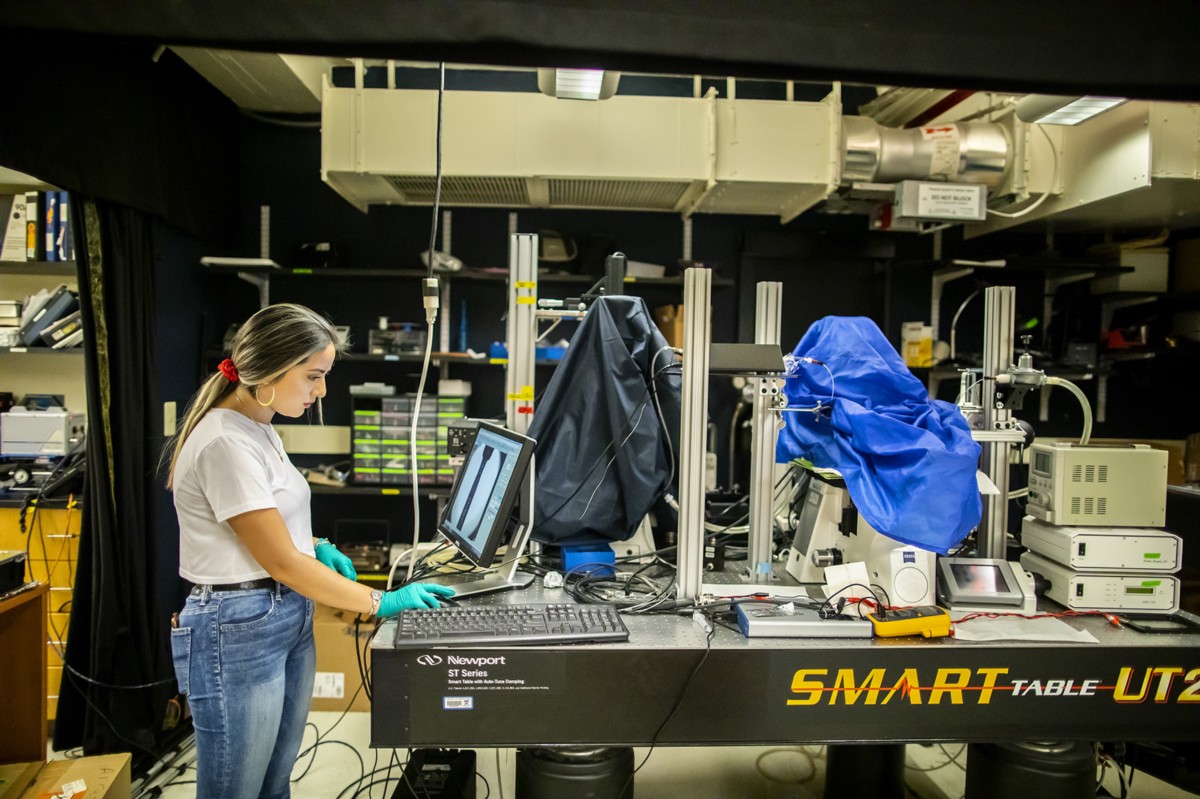 Angelica Padilla works at a computer station on a lab bench piled with electronic equipment.