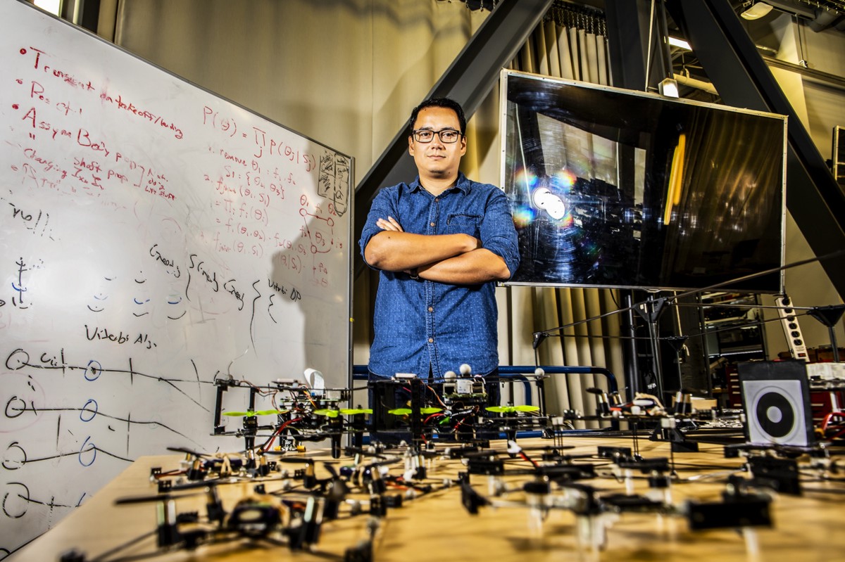 Postdoctoral researcher David Saldaña poses in front of a fleet of small flying robots.