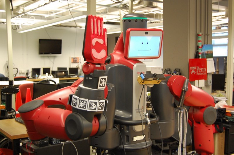 A red humanoid robot holds up its hand for a high-five. A smile is displayed on the screen that serves as its face.
