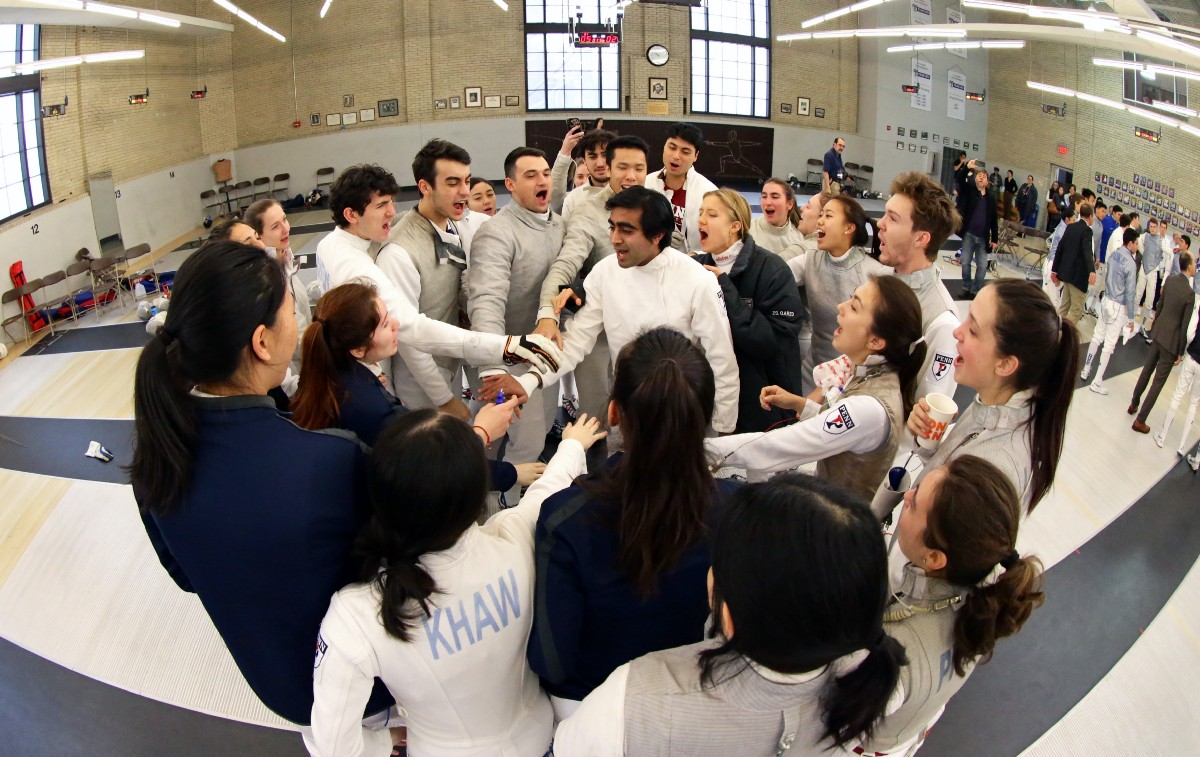 Akshay Malhotra stands in the center of a Penn Fencing team huddle.