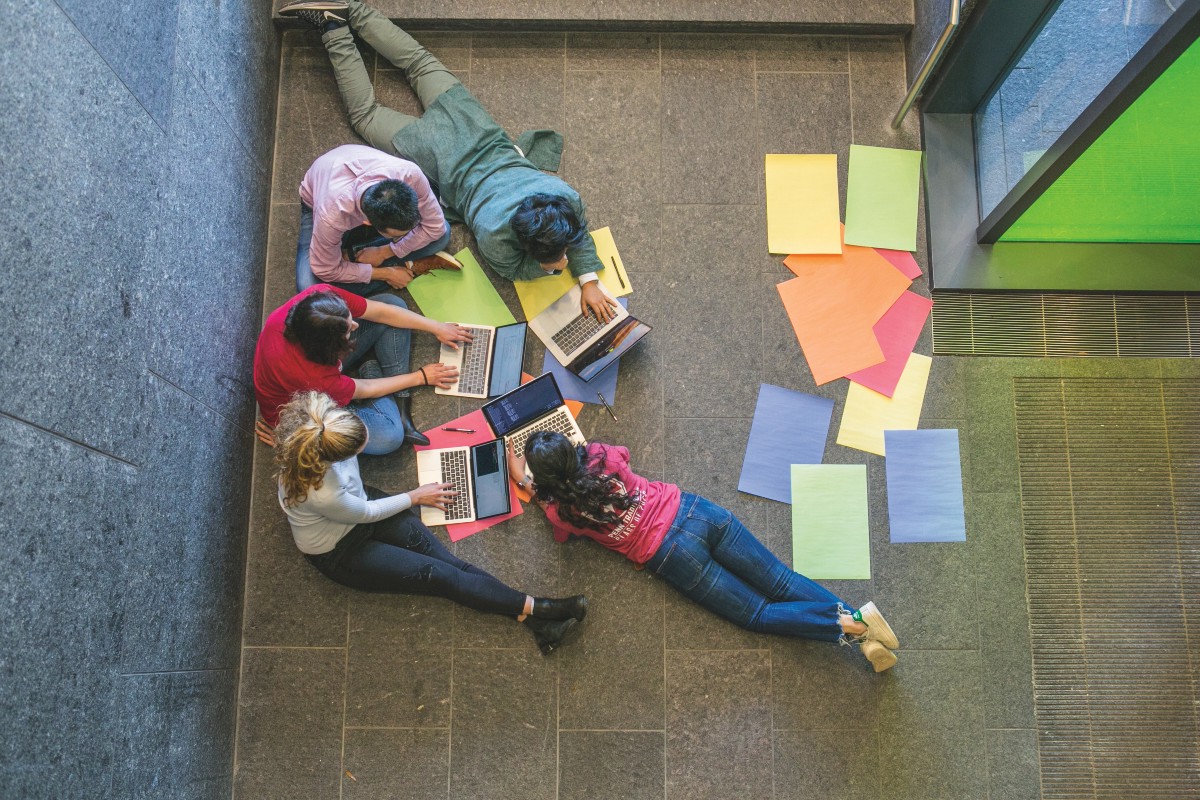 Students sit on the floor in lobby of Skirkanich Hall, working with laptops and construction paper.