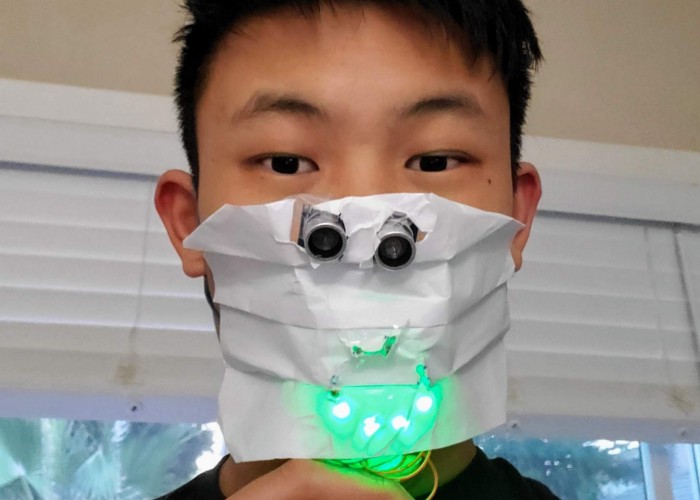 Student models DIY paper facemask with sensors and green LED lights in shape of a "smile"