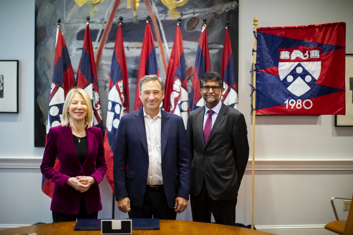 Amy Gutmann, Harlan Stone and Vijay Kumar stand in front of Penn flags and a class of 1980 banner.
