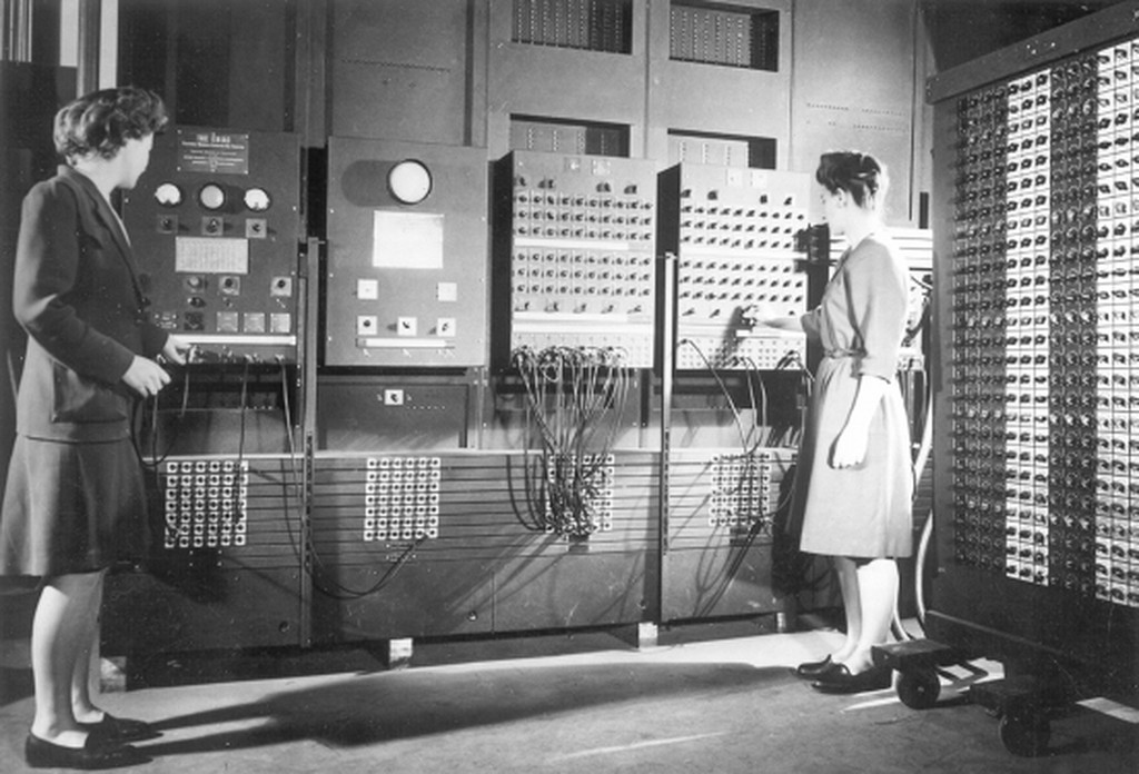 An archival photo of two women, Jean Bartik and Frances Spence, operating the ENIAC’s main control panel, a massive, complicated array of dials and wires.