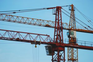 Two red construction cranes against blue sky background