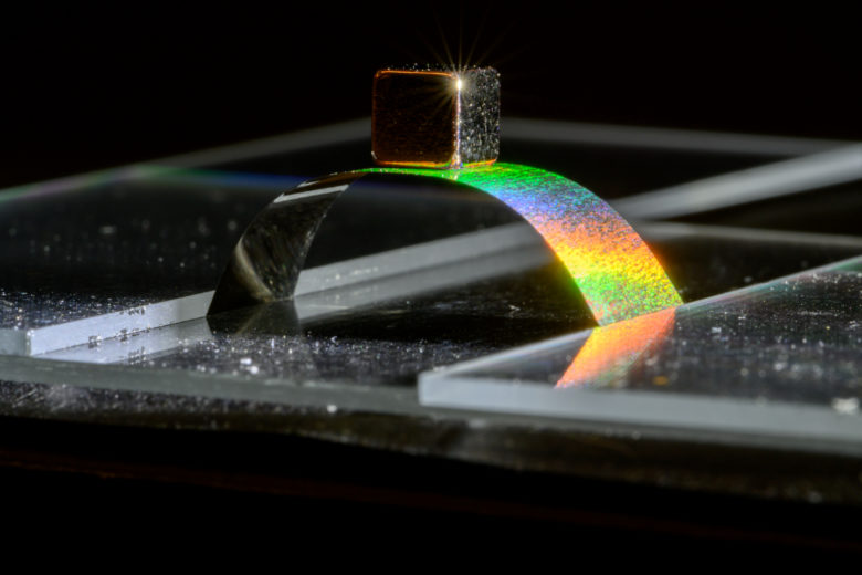 A weighted cube balances on a glimmering arch of thin metal.