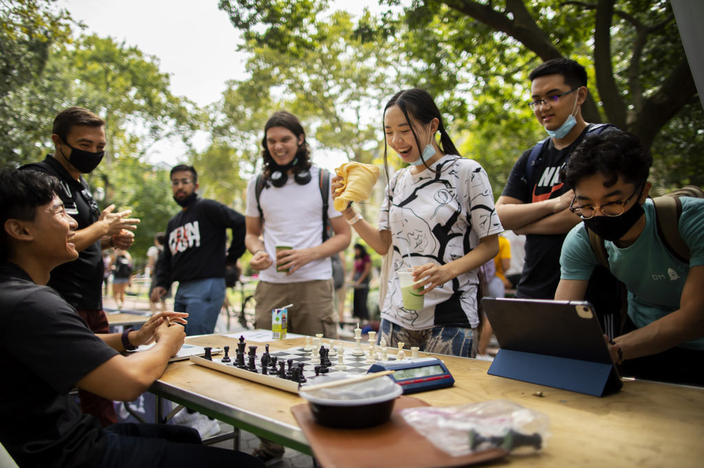 Students gather around a chessboard at an outdoor extracurricular fair.