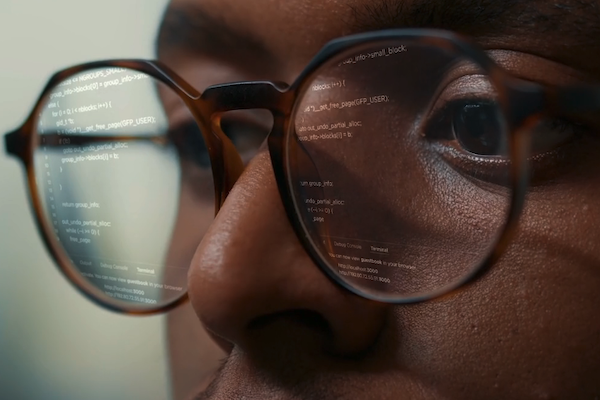 Close up of a person's face with computer code reflected in their glasses