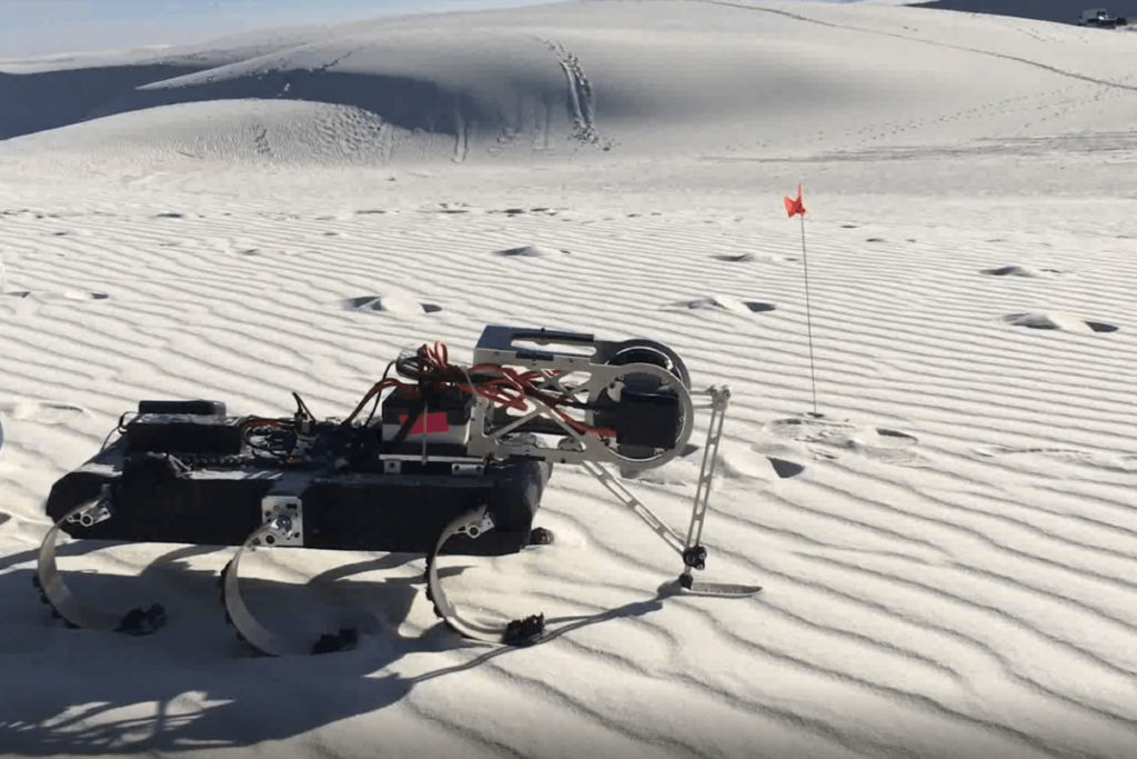 A six-legged robot walks in the dessert.