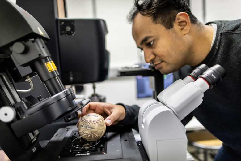 Postdoctoral researcher Shravan Pradeep puts a muddy baseball under a microscope to see what properties the mud has.