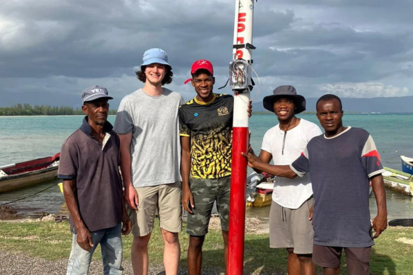 Five young men hold a red and white buoy in front of a Jamaican beach.