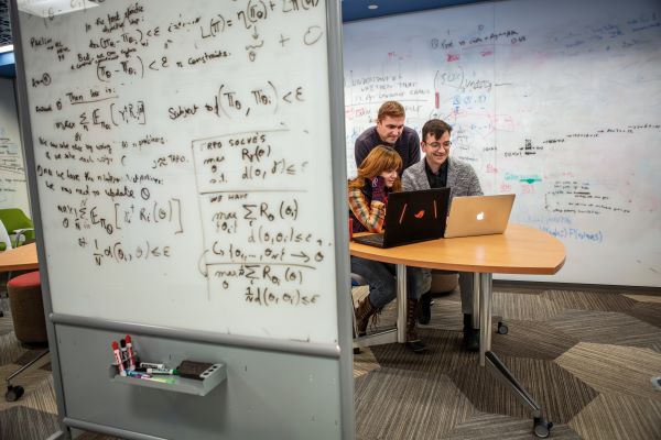 Professor Chris Callison Burch is sitting at a desk with a computer that has students surrounding him.