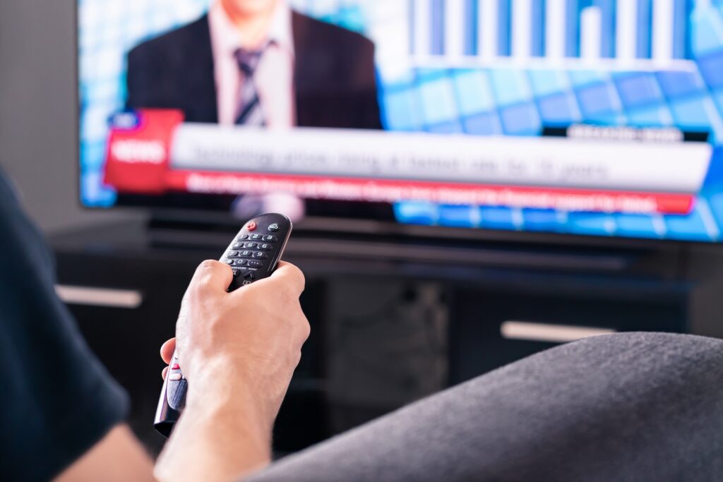 Picture of a person holding a remote while watching a political debate on TV