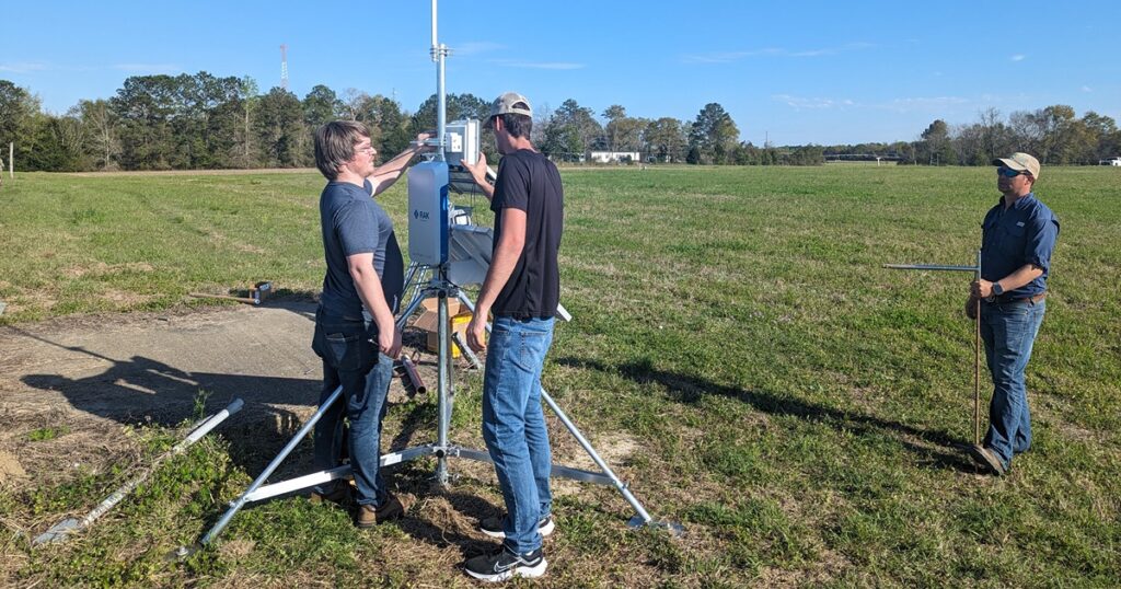 Men standing in a farming field utilizing their new sensor equipment to help provide real time data to farmers.