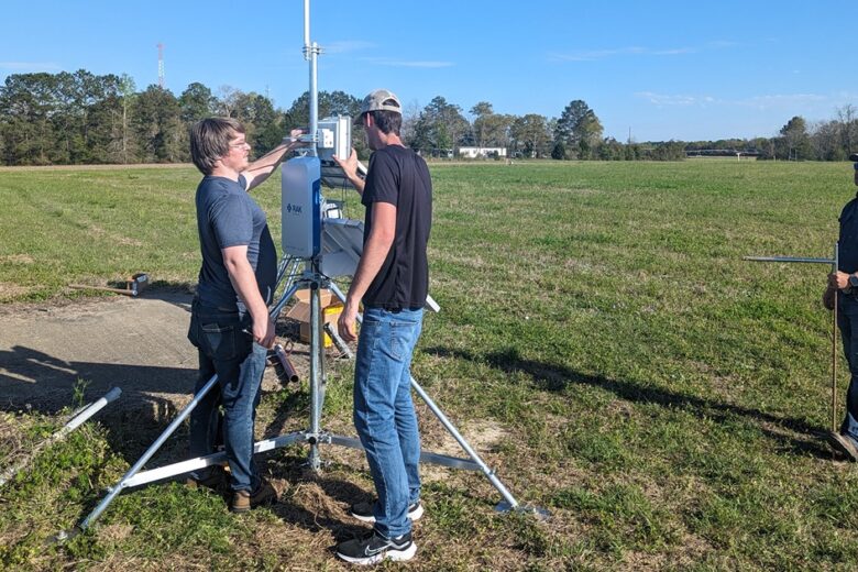 Men standing in a farming field utilizing their new sensor equipment to help provide real time data to farmers.