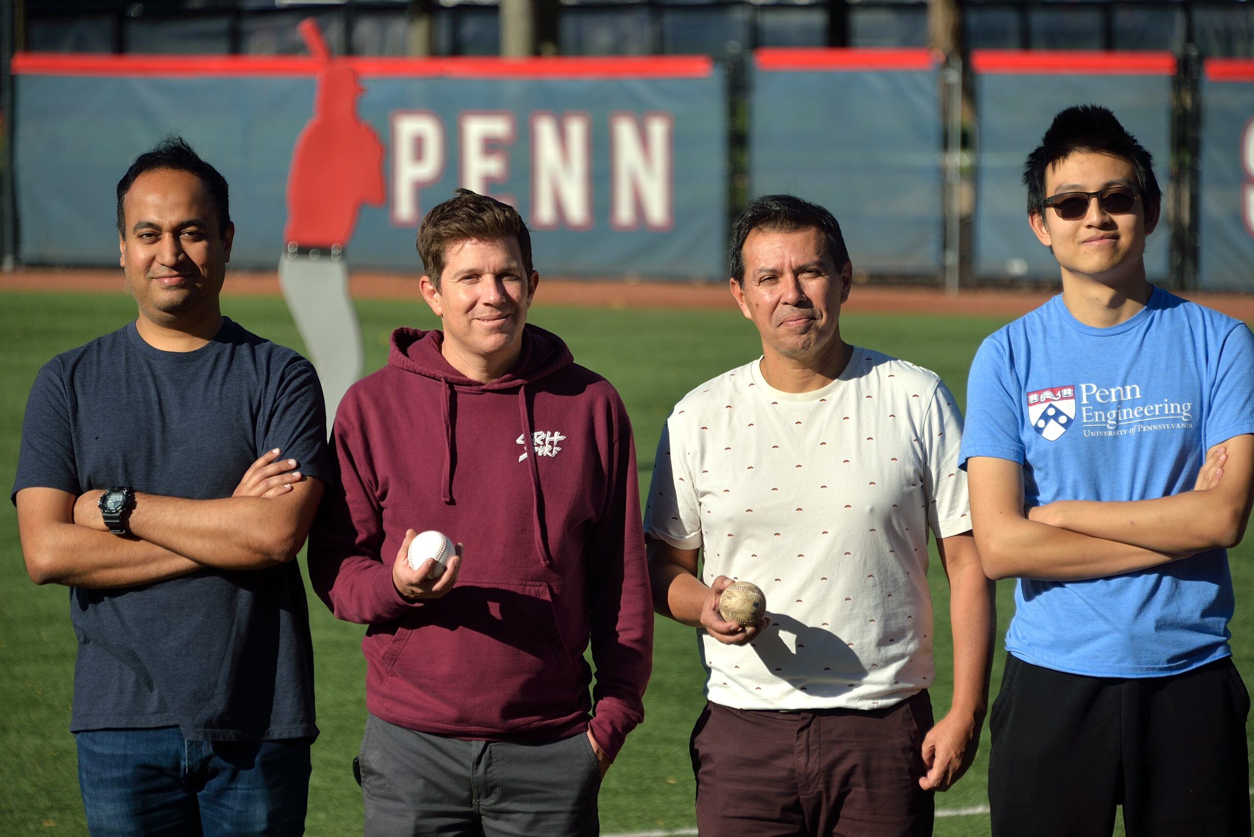 A group of male researchers stand in a baseball field facing the camera.