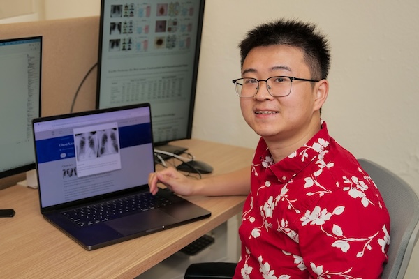 Yue Yang sits at a computer wearing a Hawaiian shirt. 