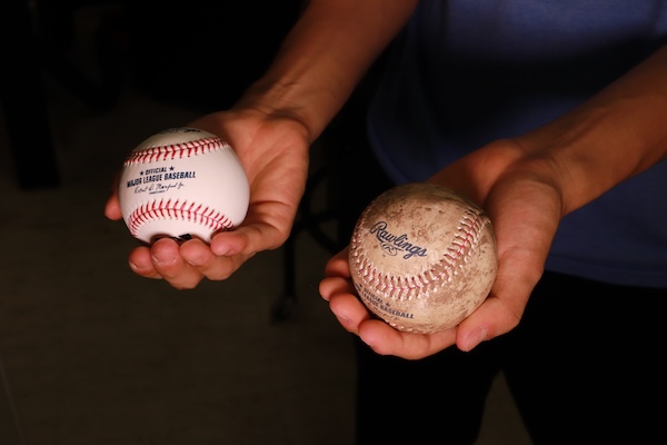 A pair of hands hold two baseballs, one coated in mud, the other pristine.