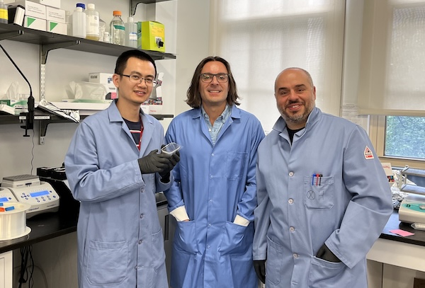 A group of three researchers stand side by side in a lab.