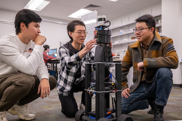 Three researchers squat near a robot.