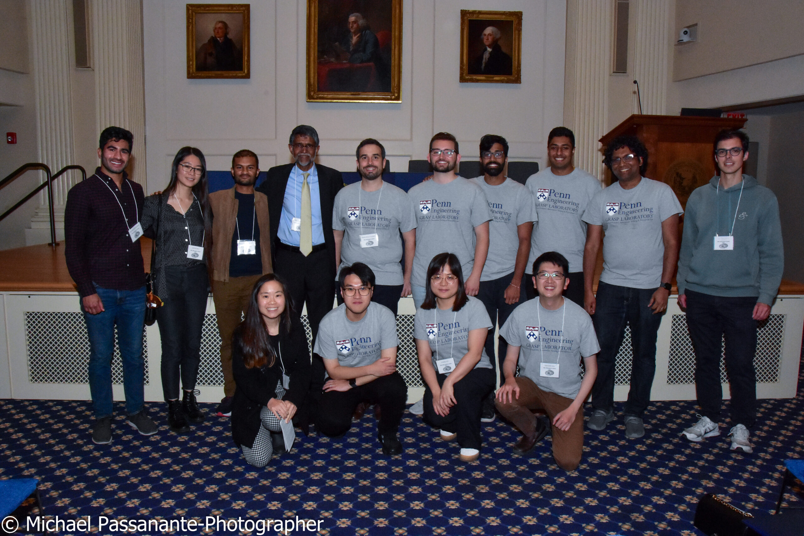 Awardee Vijay Kumar stands beneath a portrait of Benjamin Franklin, flanked by some of his many graduate students.