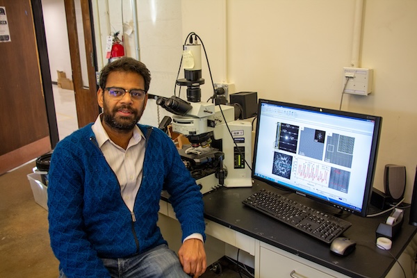 Ritesh Agrawal poses next to a microscope used in his research.