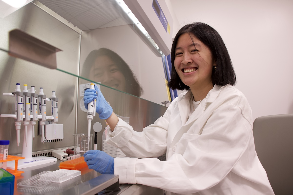 A woman in a white lab coat uses a micropipette