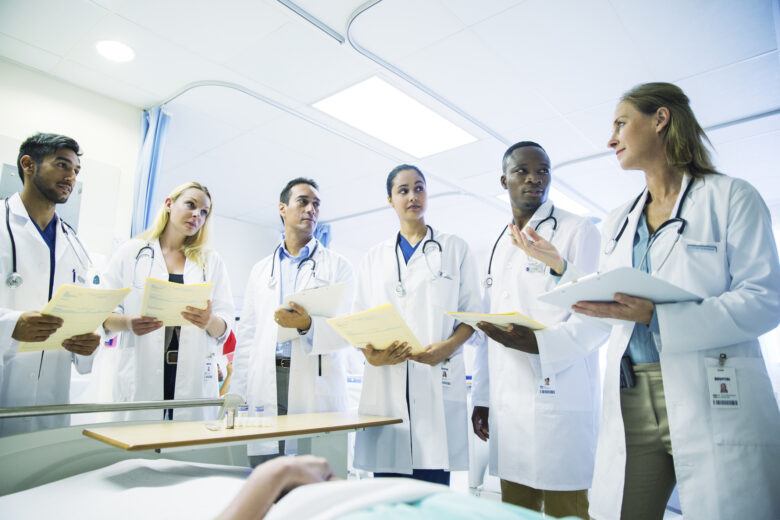 Doctors reviewing charts together at the bedside of a patient.