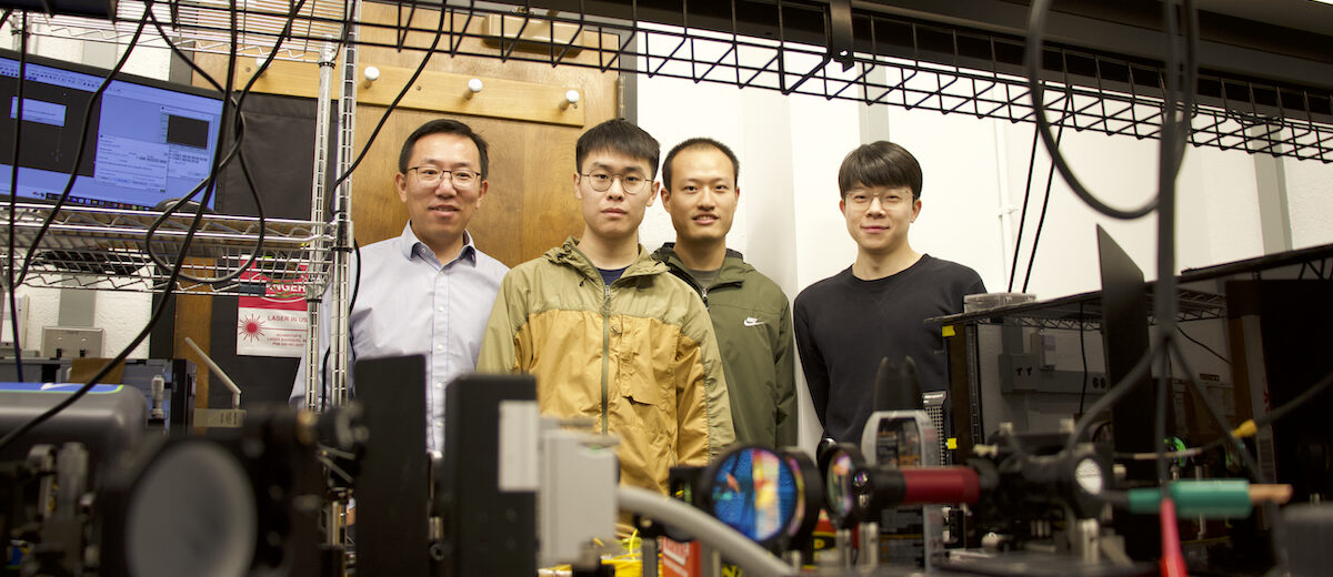 A quartet of male researchers stands behind their lab equipment, which includes mirrors and cameras.