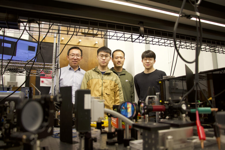 A quartet of male researchers stands behind their lab equipment, which includes mirrors and cameras.