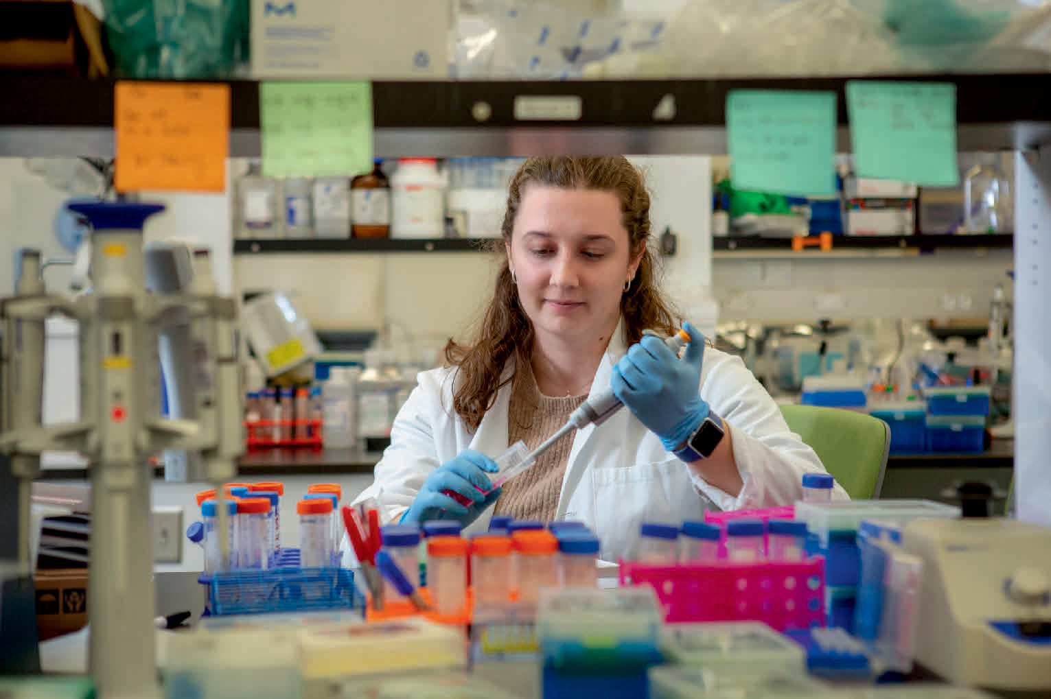 A woman wearing a lab coat uses a micropipette.