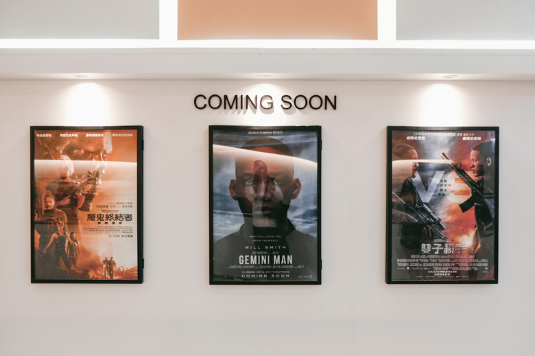 Three movie posters stand side by side in a theater, under a "Coming Soon" sign.