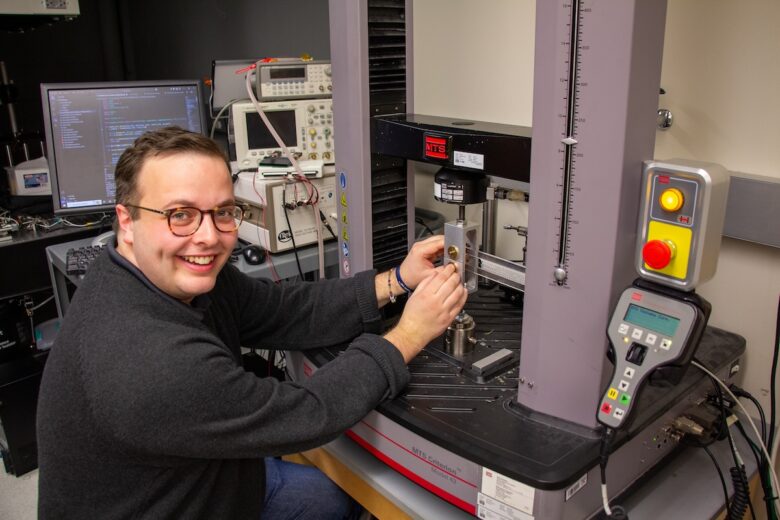 A male researcher in a black sweater looks at the camera while operating a machine.