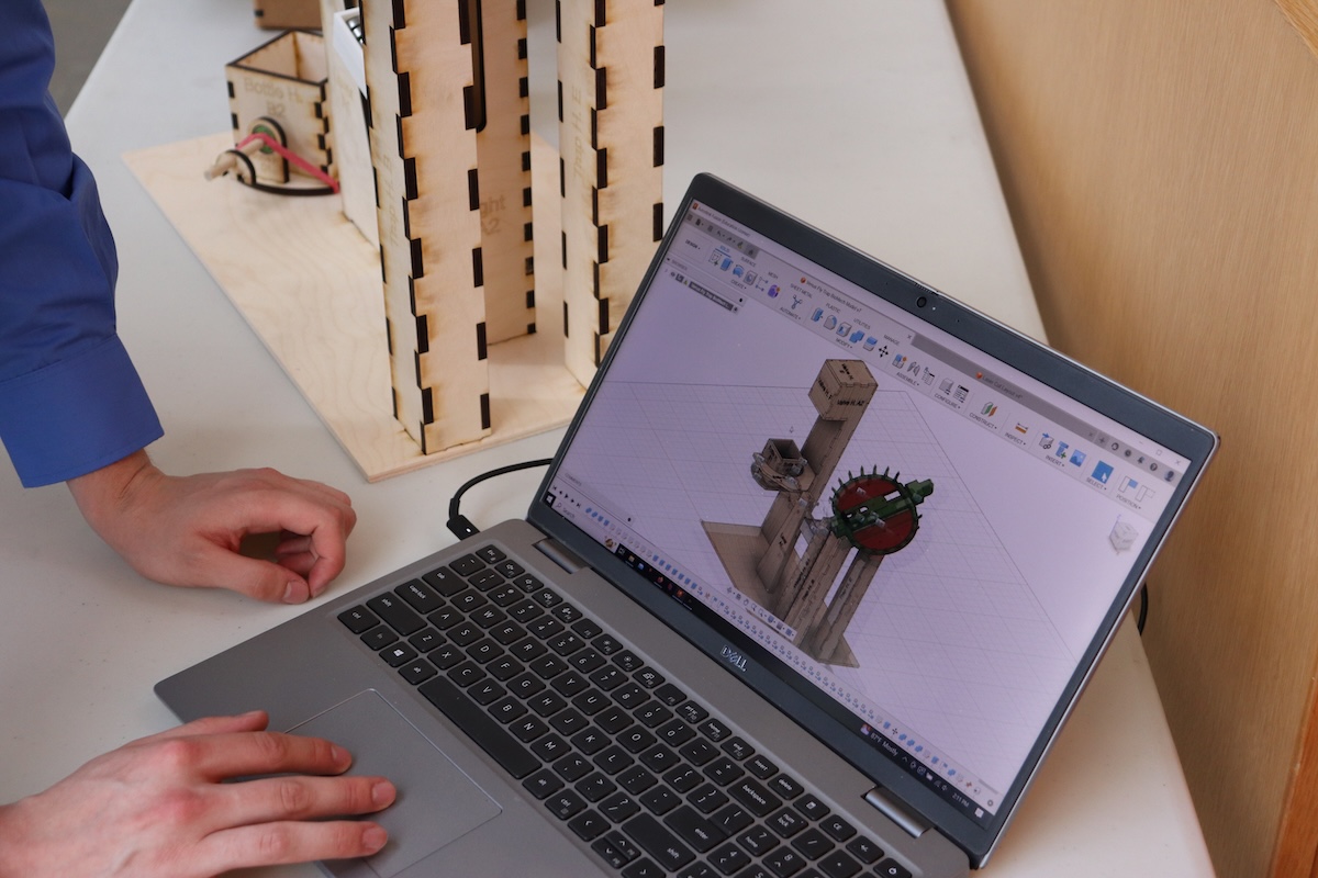 A laptop displays a digital model of a Venus flytrap mechanism made of wood and plastic, next to the finished result.