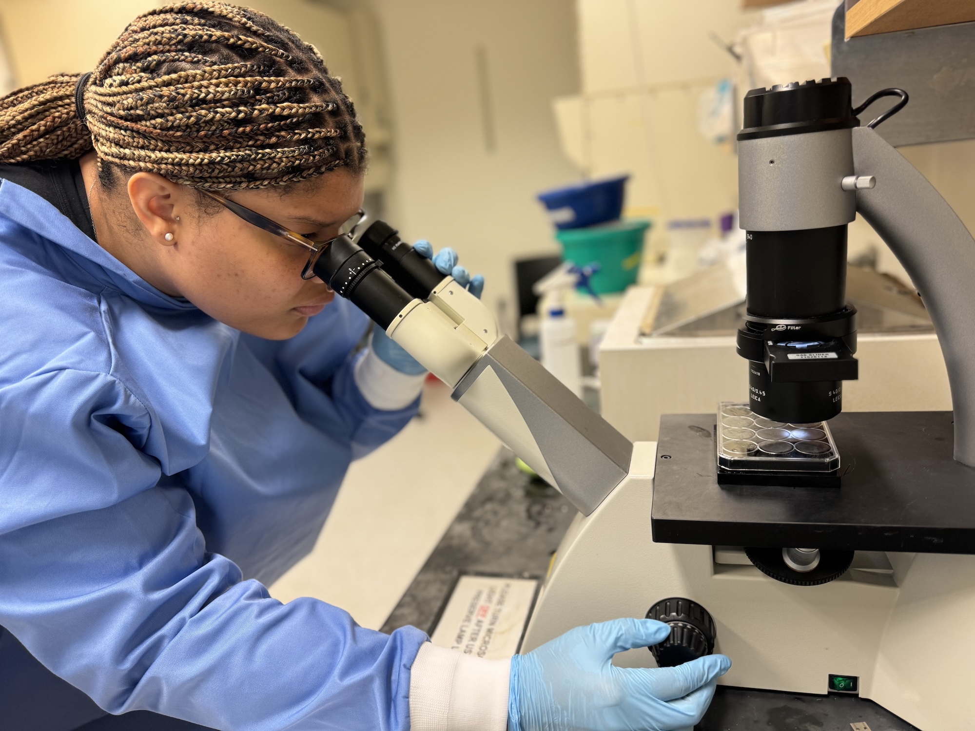 A woman in a lab coat peers through a microscope. 