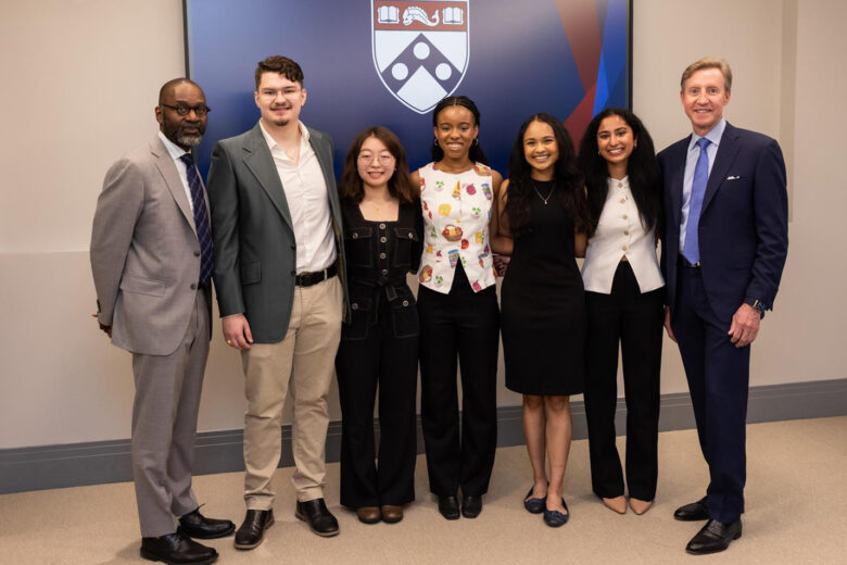 A picture of student prize winners in front of a screen with the Penn logo. From left to right, the people are as follows:(From left) Provost John L. Jackson Jr, Jack Roney, Ejun Mary Hong, Imani Nkrumah Ardayfio, Inaya Zaman, Rashmi Acharya, and Penn President J. Larry Jameson.