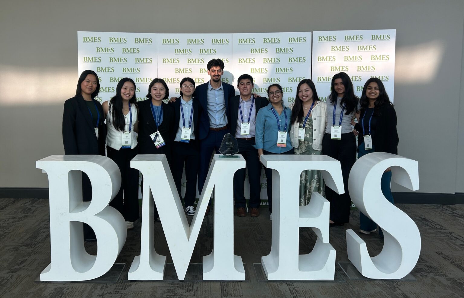 A group of students pose behind a large sign that reads "BMES"