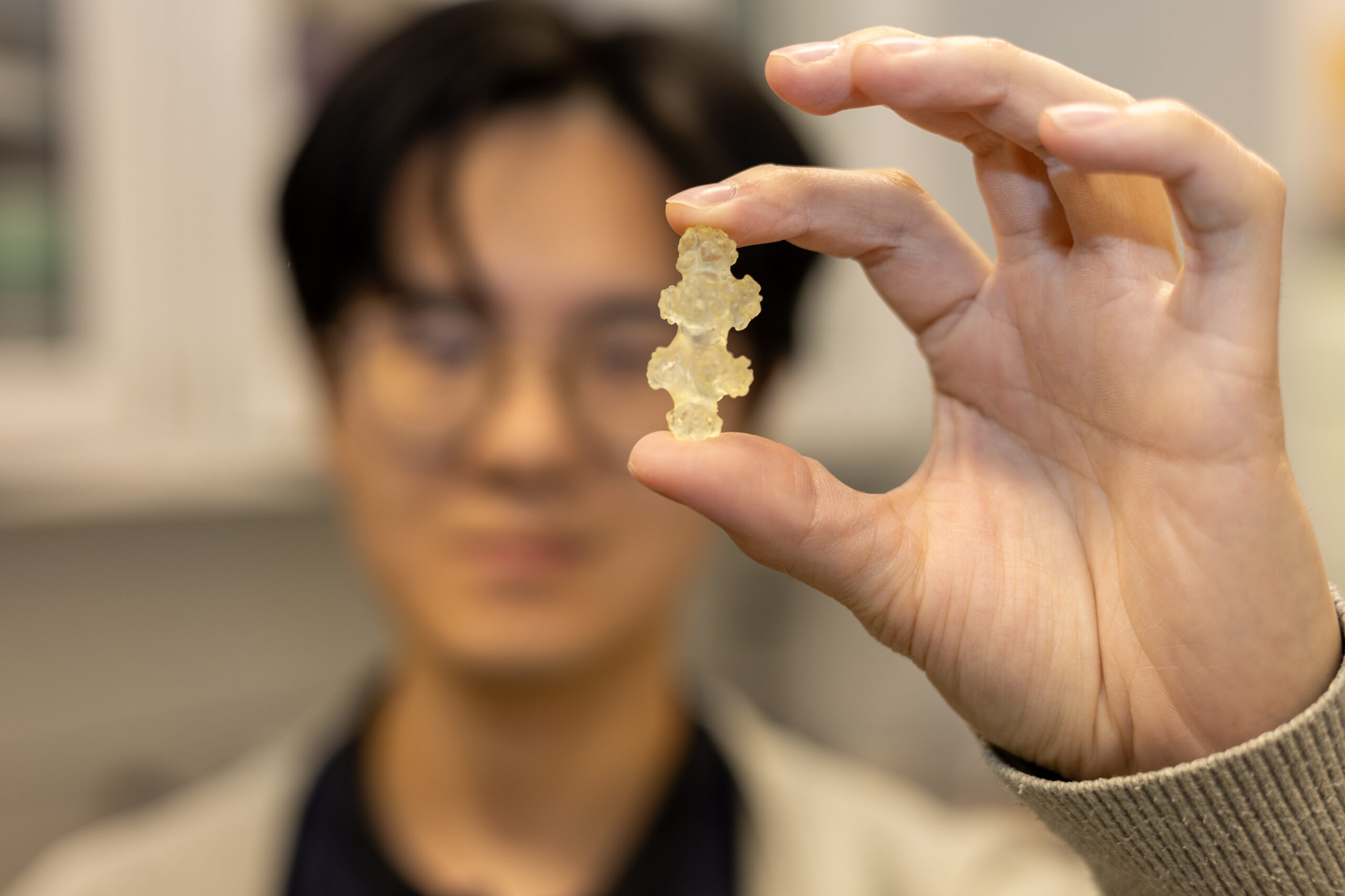 A researcher holds a small 3D printed piece of plastic close to the camera. 
