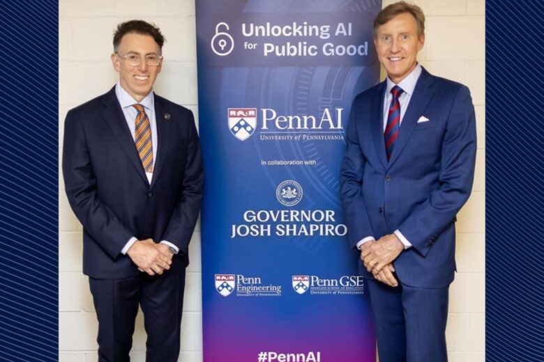 Two men in suits stand framing a poster.