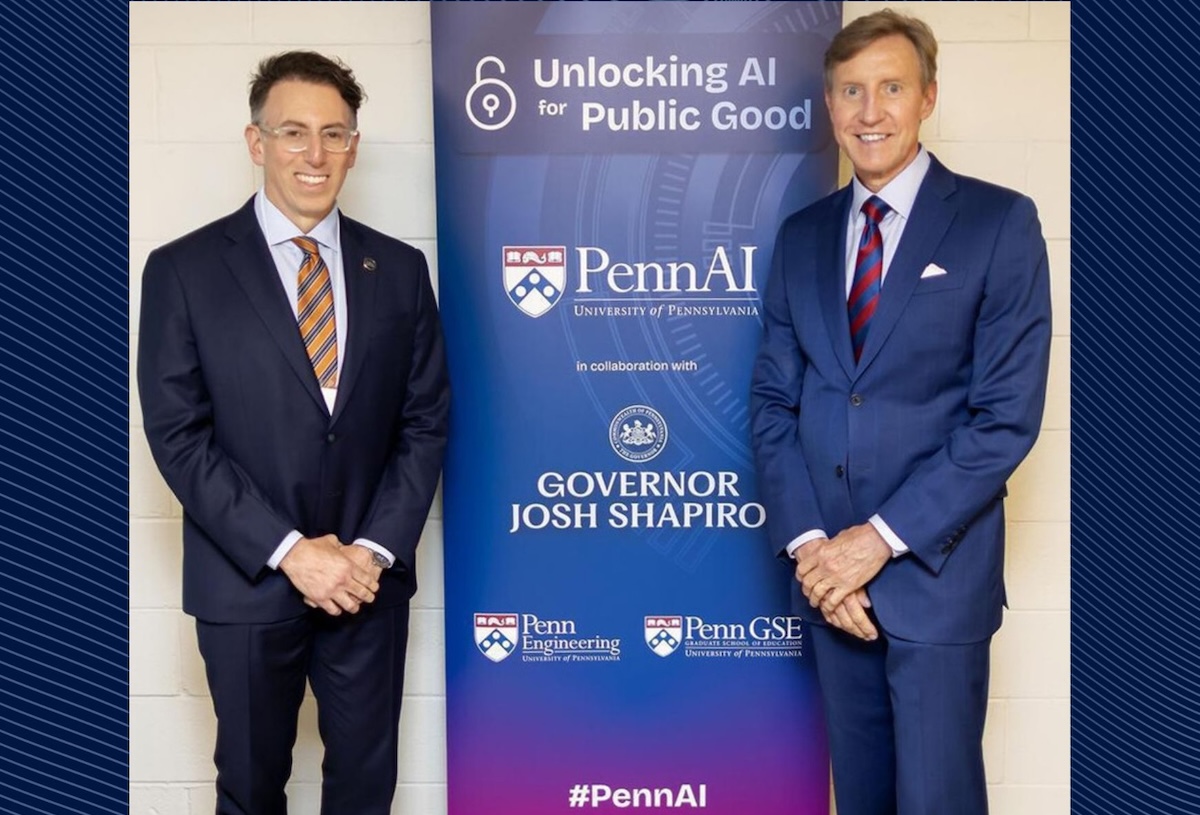 Two men in suits stand framing a poster. 