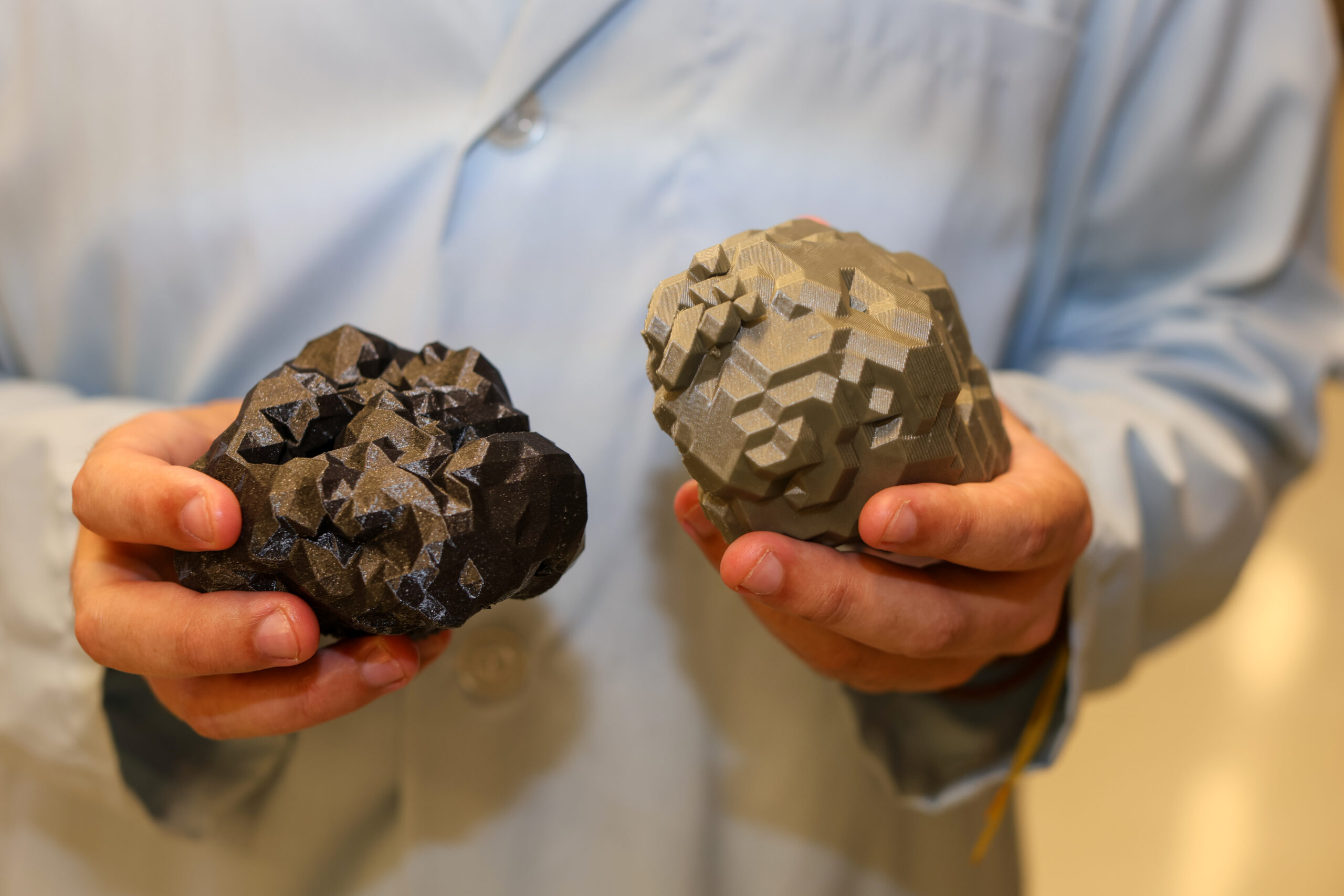 A pair of hands hold two 3D printed nanoparticles.
