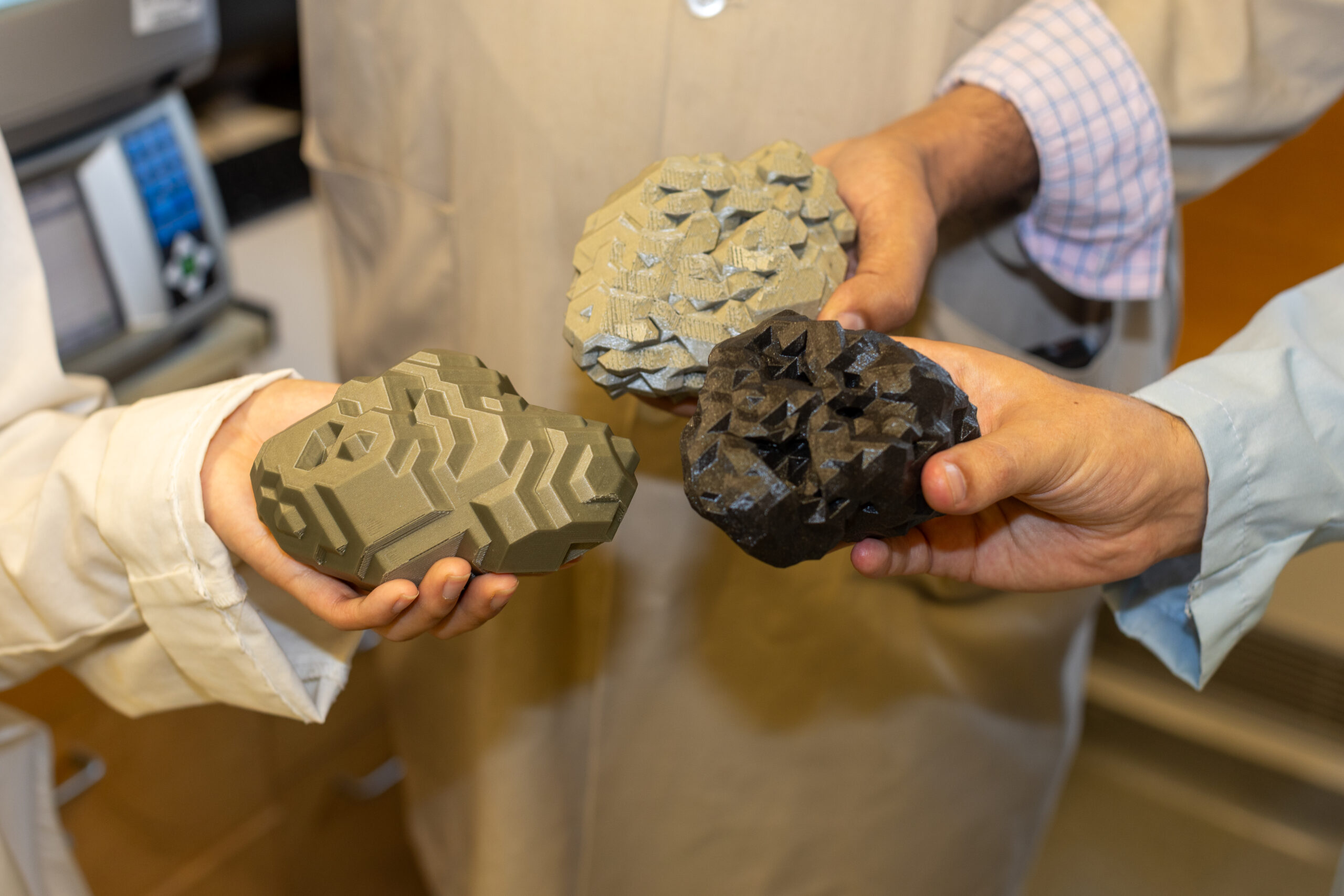 A trio of hands holding 3D-printed nanoparticles.