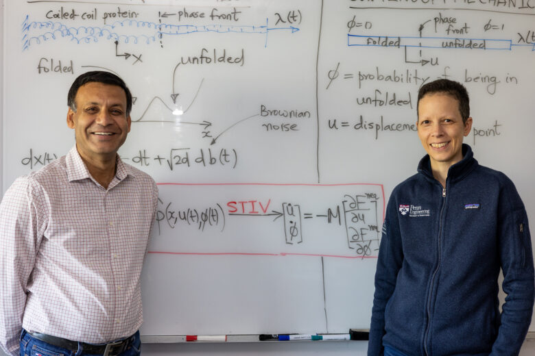 Two researchers, one male and one female, stand in front of a whiteboard covered in mathematical equations.
