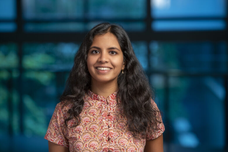 A woman with long dark hair poses in front of a window.